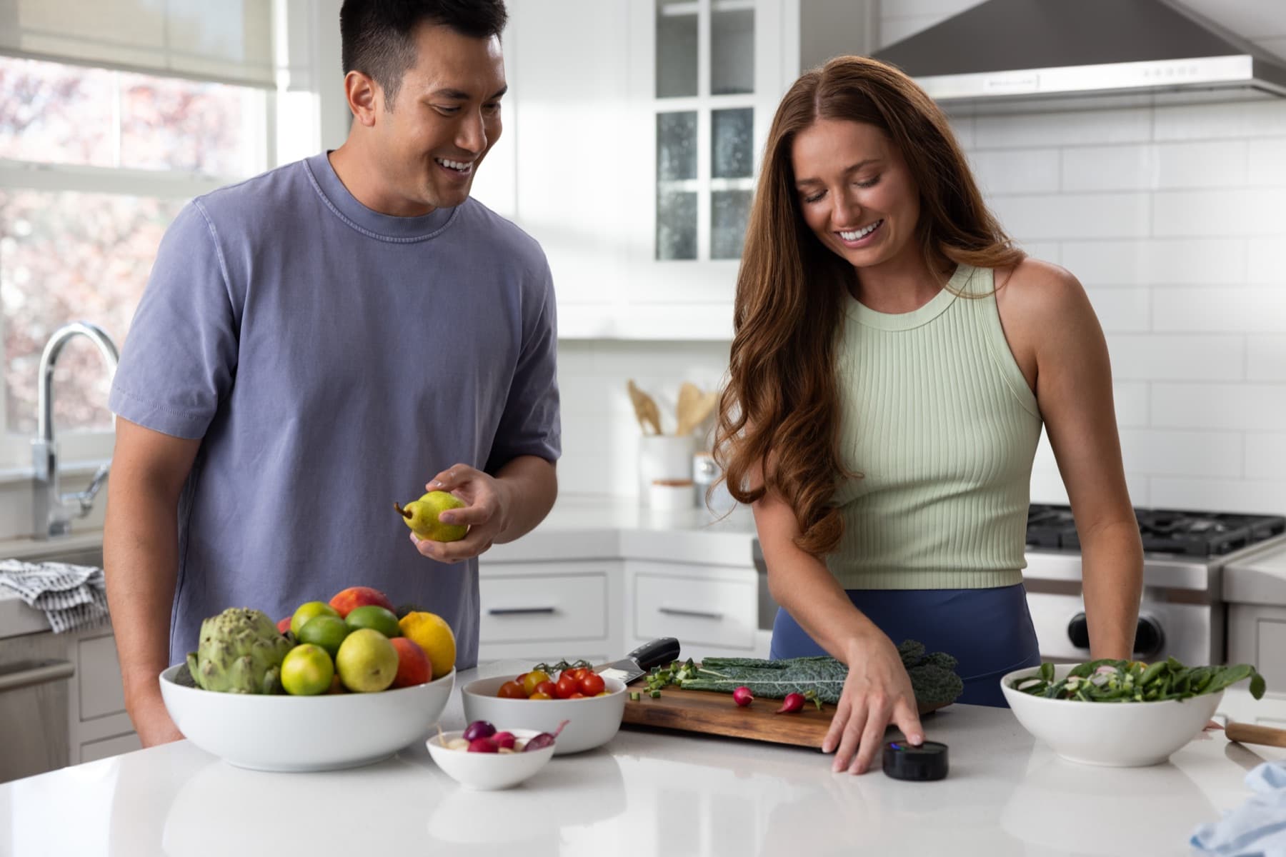 Two people laughing at a kitchen counter as one rests a fingertip on the Prysm iO scanner