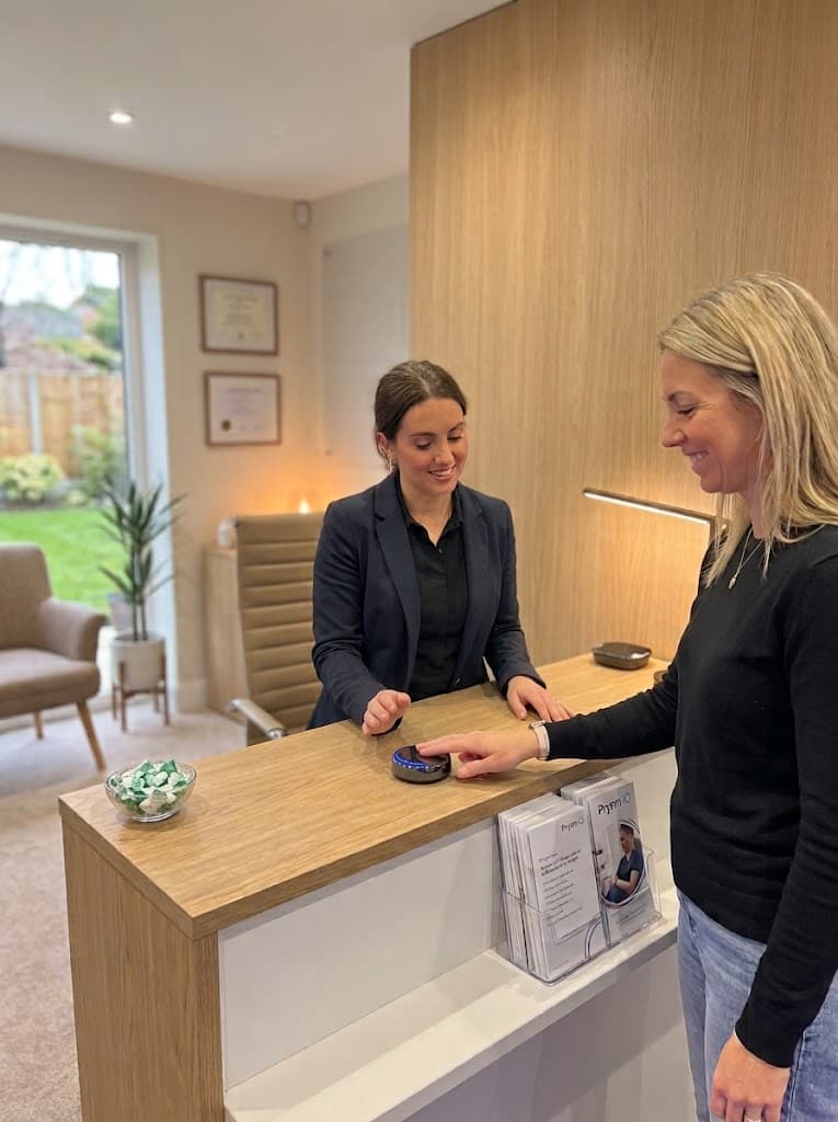 Someone with a fingertip on the Prysm iO scanner at a practice reception desk as a colleague looks on